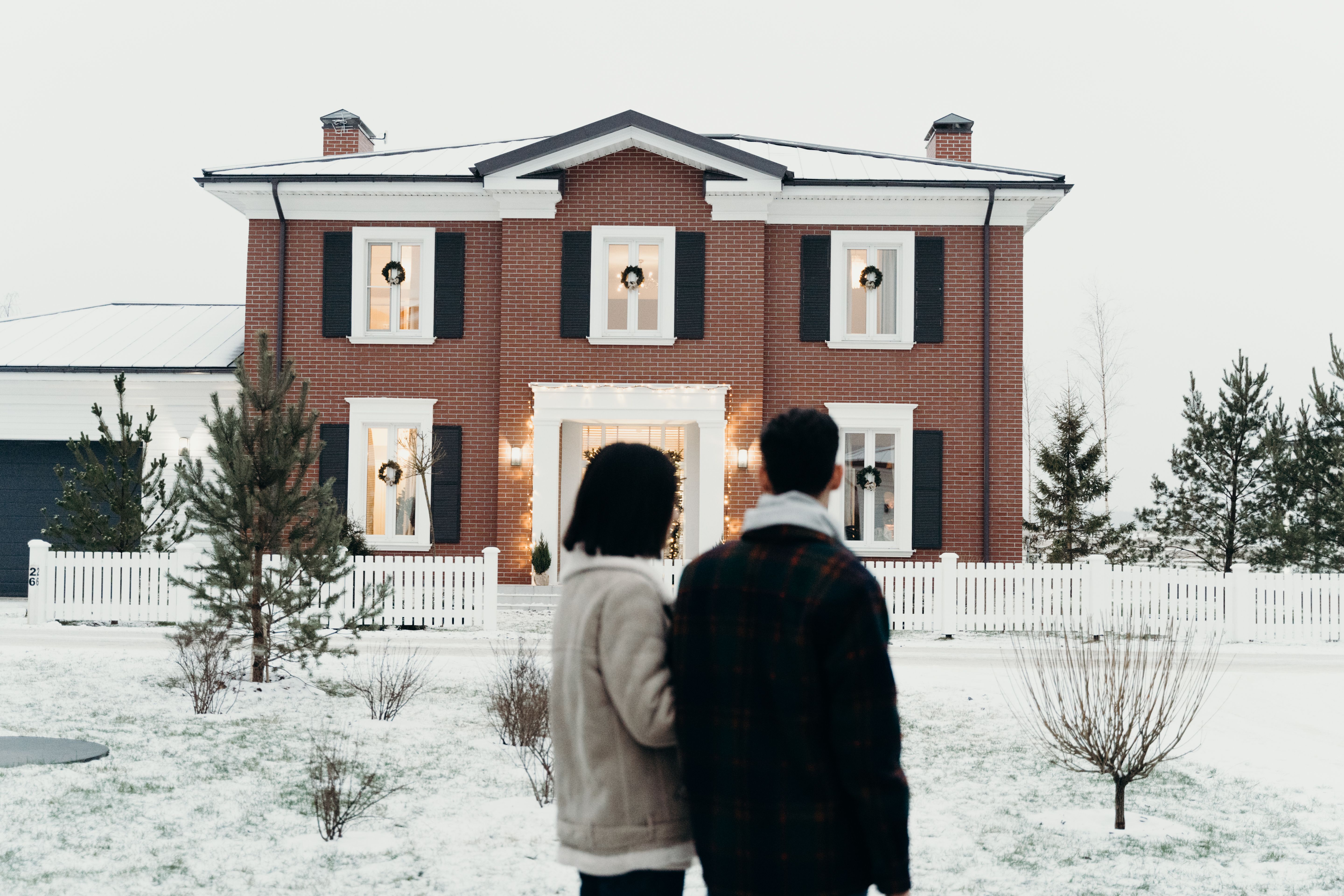 a-couple-stands-admiring-a-brick-house-decorated-for-winter,-surrounded-by-snow. - cottonbro-studio (pexels)
